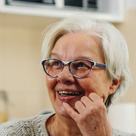 An older woman in glasses smiling, chin resting on her hand