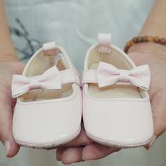 A pair of tiny white baby shoes with bows held in two hands