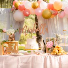 A pastel dessert table set up outdoors under a balloon arch for a baby shower