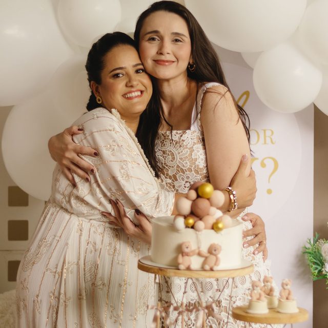 Two women hugging behind the cake at a baby shower hung with balloons