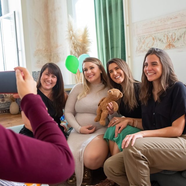 A guest photographing four friends sitting together on a sofa at a baby shower