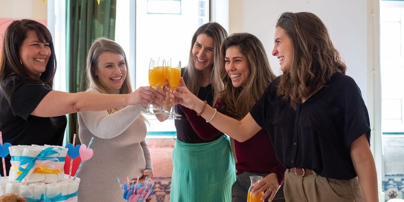 Friends reaching in to touch glasses of juice over a baby shower table