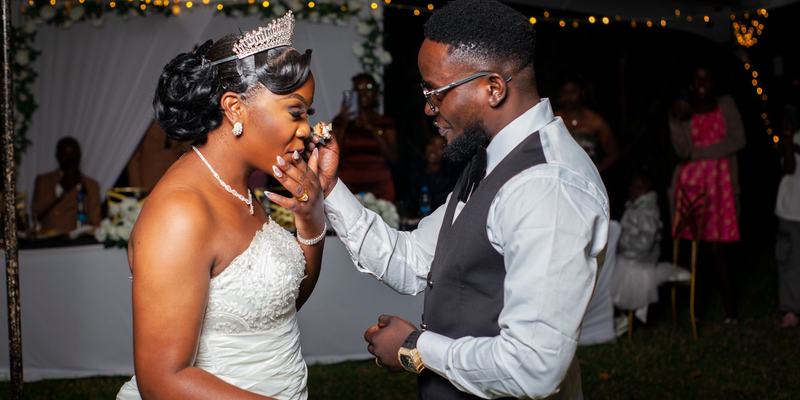A bride feeding the groom a bite of wedding cake at an outdoor reception after dark