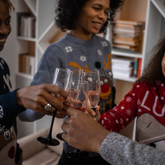 Hands in Christmas jumpers touching glasses together at home