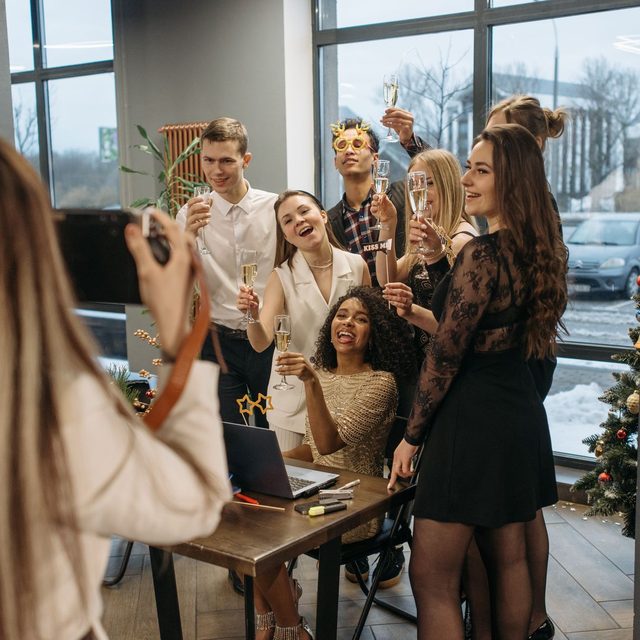 A woman photographing colleagues on her phone as they raise their glasses