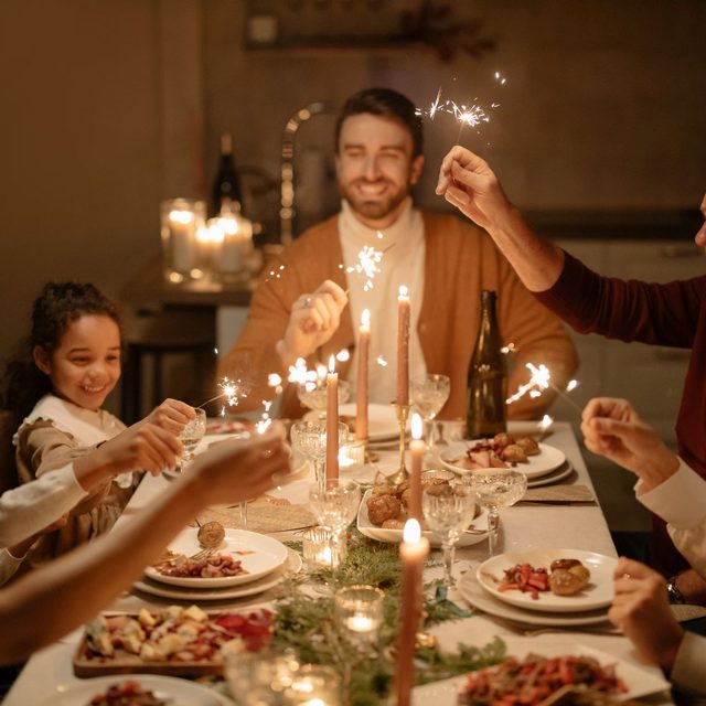 A family holding sparklers over a candlelit Christmas dinner table