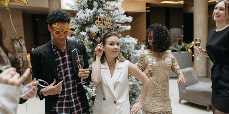 Guests with drinks moving around a party room beside a frosted Christmas tree