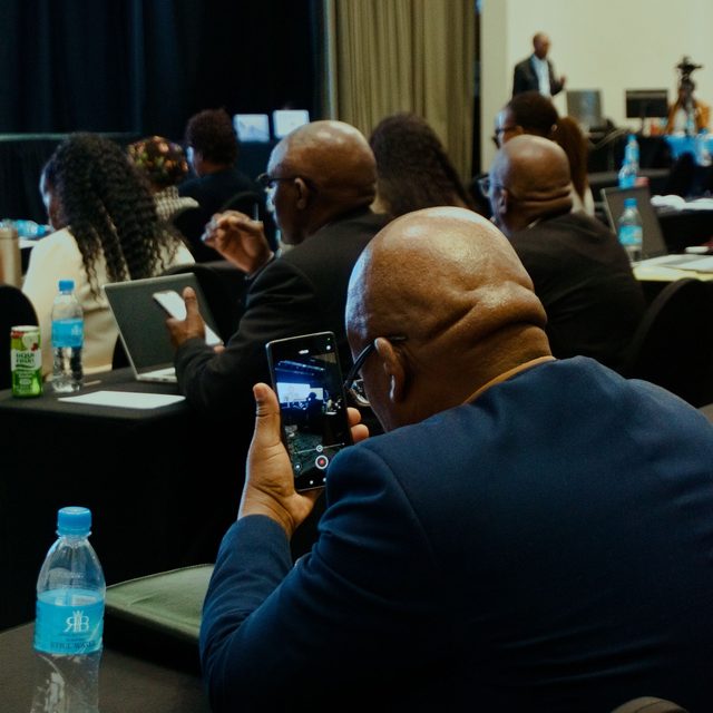 An attendee photographing the stage on their phone from the back of a conference room