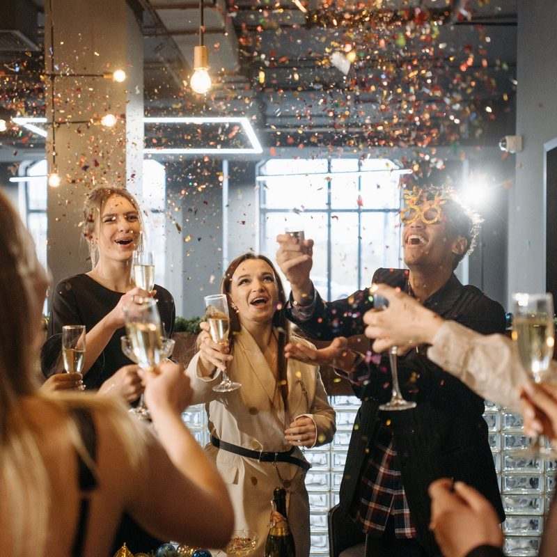 Colleagues raising champagne glasses under a burst of gold confetti at a company party