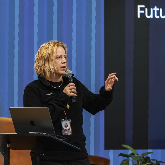A woman speaking into a handheld microphone beside a projected conference slide