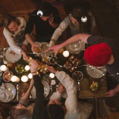 Overhead view of friends reaching across a dinner table strung with lights