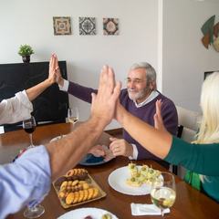 Older friends high-fiving across the table at a dinner party