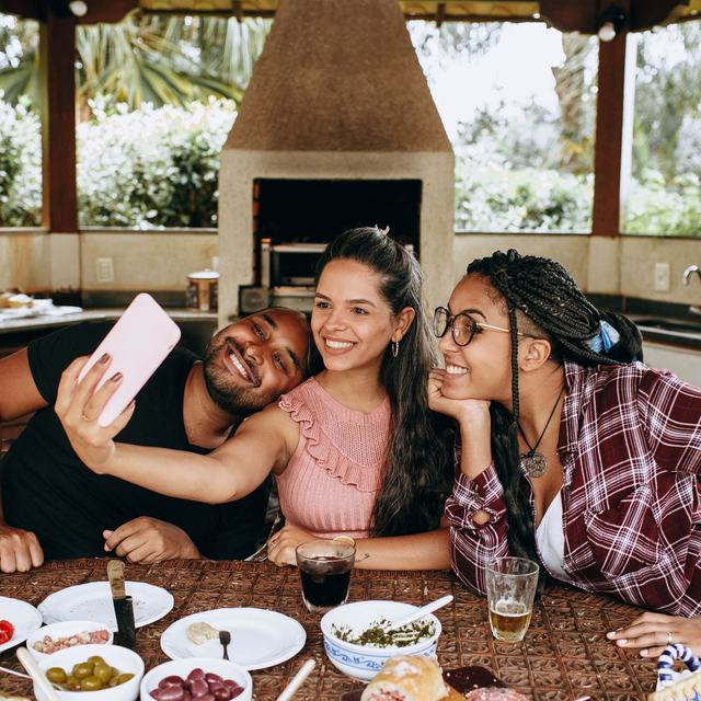 Three friends squeezing into a phone selfie over a table of half-finished food