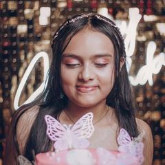 A girl smiling with her eyes closed behind a pink butterfly birthday cake