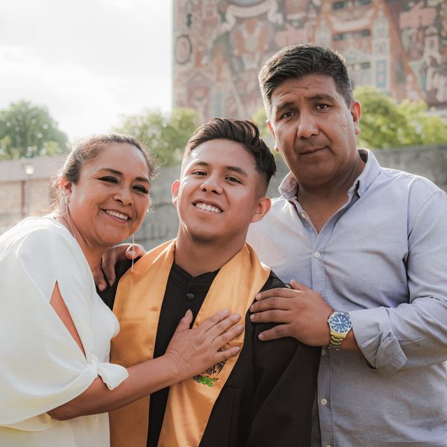 A graduate standing between their mother and father outside the ceremony