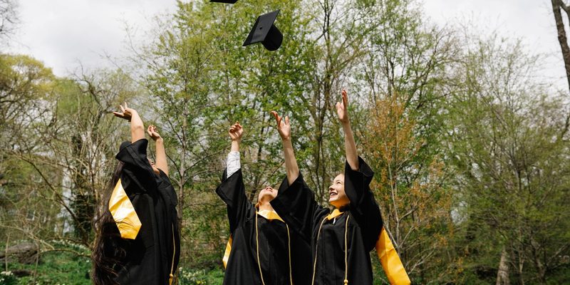 Graduates throwing their mortarboards into the air under trees