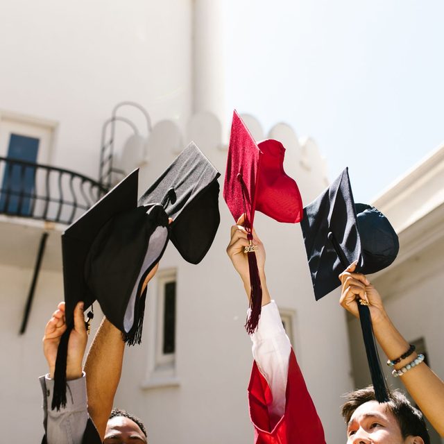 Mortarboards and hoods held up against a white building on graduation day