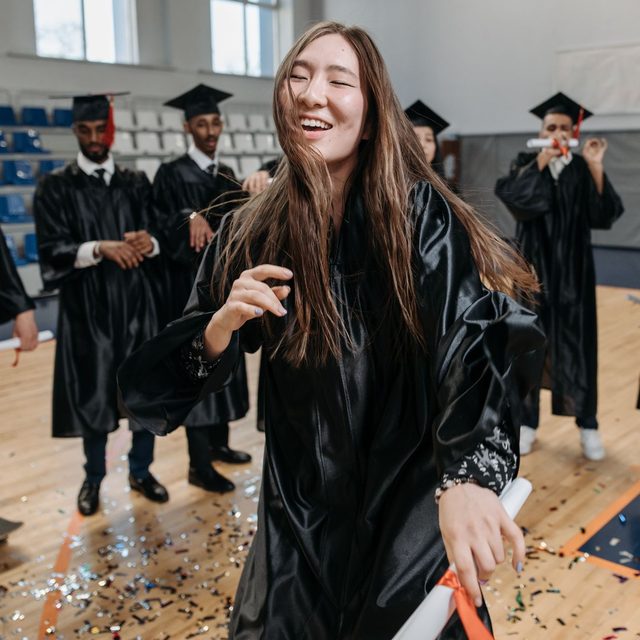 A graduate laughing in the middle of a ceremony hall covered in confetti