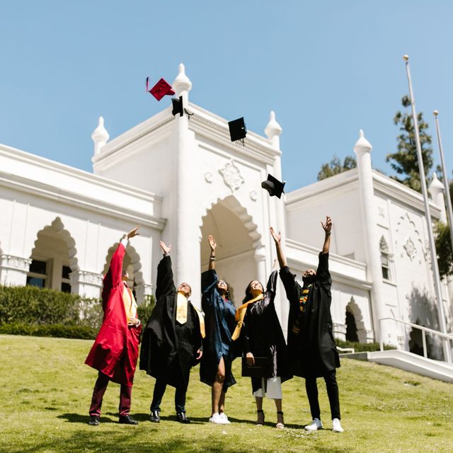 A group of graduates on the lawn throwing their caps outside the hall