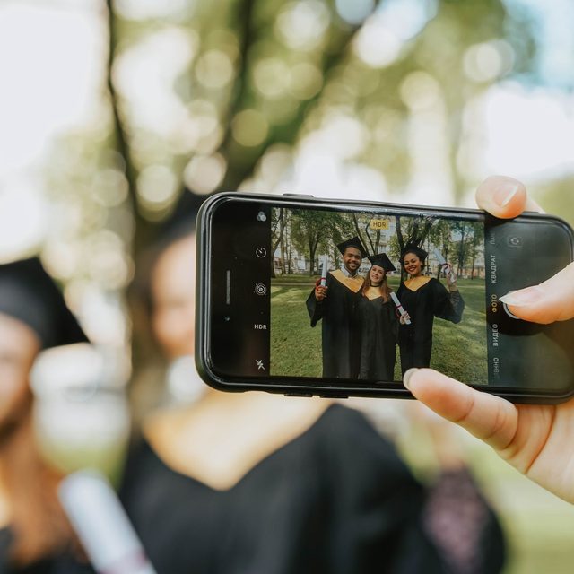 A phone held up at arm’s length, framing a group of graduates on its screen