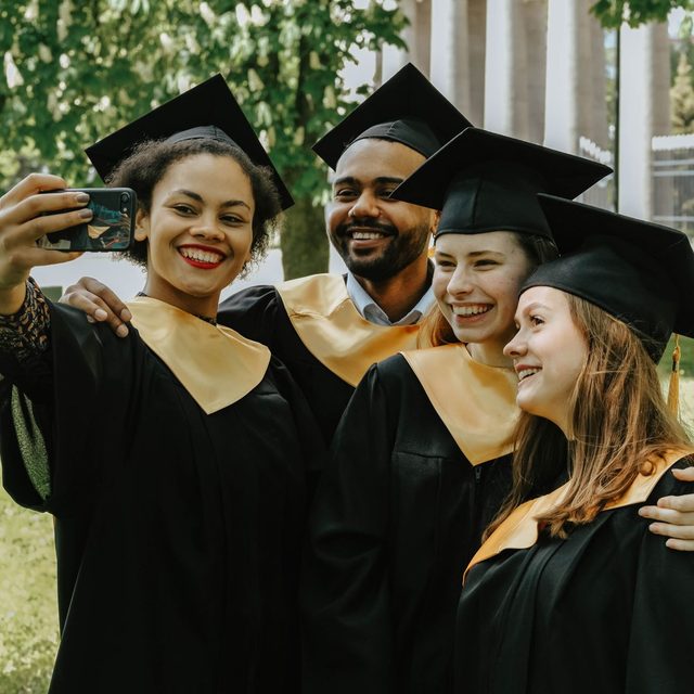 Four graduates crowding into a phone selfie in their caps and gowns