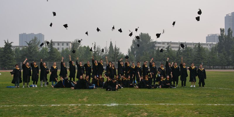 An entire year group lined up on a field with their caps in the air above them