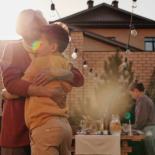 A grandmother hugging her grandson in a sunlit backyard before a family meal
