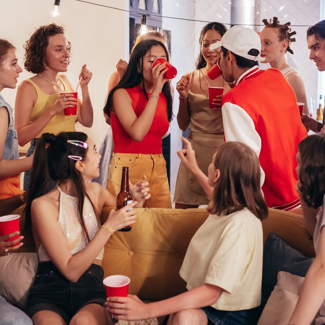 A living room packed with friends holding drinks at a house party