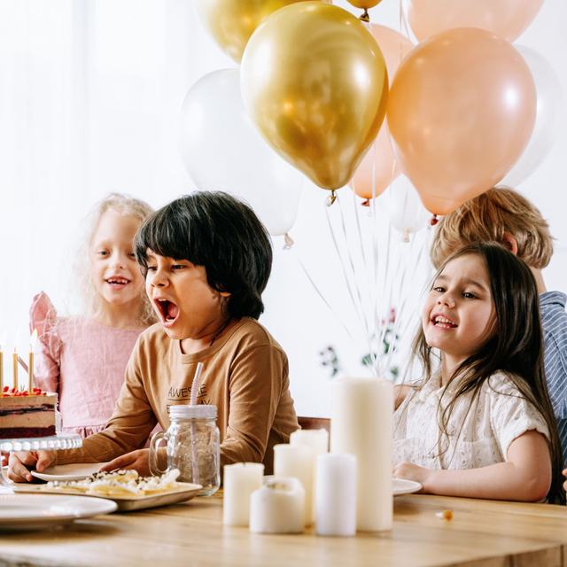 Two children pulling faces at a table under gold and peach balloons