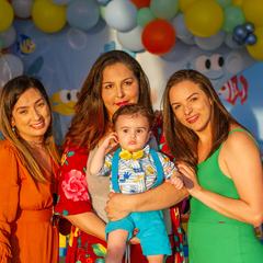 Three women holding a baby in front of a wall of colourful party balloons