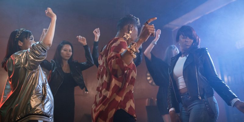 A crowd dancing with their arms up under warm lights at a party
