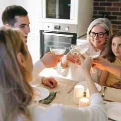 Three generations of a family clinking glasses over a candlelit kitchen table