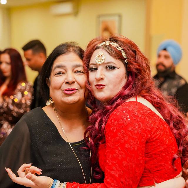 Two women in bright dresses leaning together and laughing at a wedding reception
